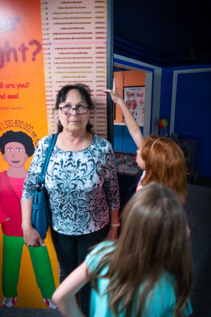 A group of people are standing in front of a colorful display at a museum. They appear to be engaged in an interactive exhibit.