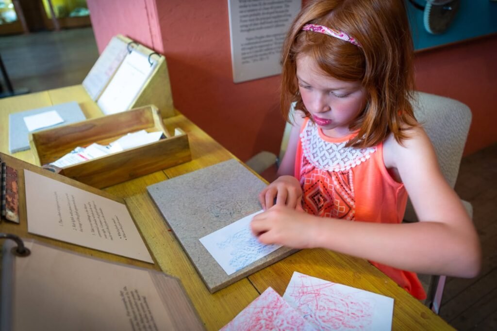 A focused young student works with patterned cards at a wooden table in a museum display.