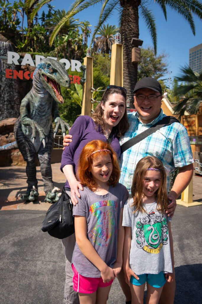 A family poses for a photo next to a T-Rex statue in front of a sign that reads Raptor Encounter.