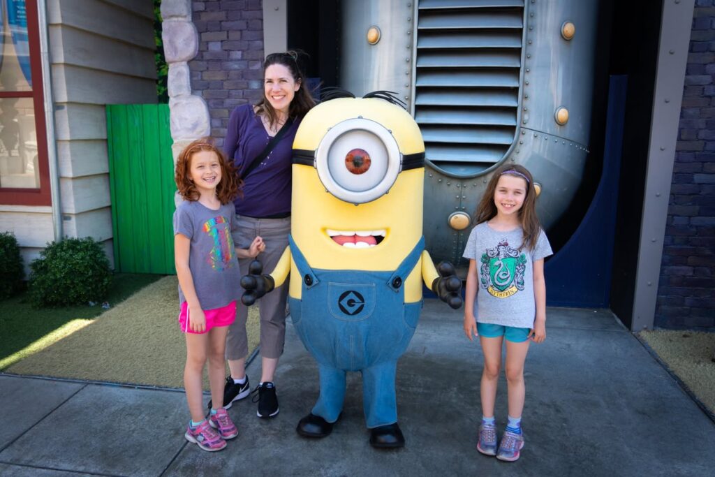 A family posing with a Minion character in an industrial-looking setting at a theme park.