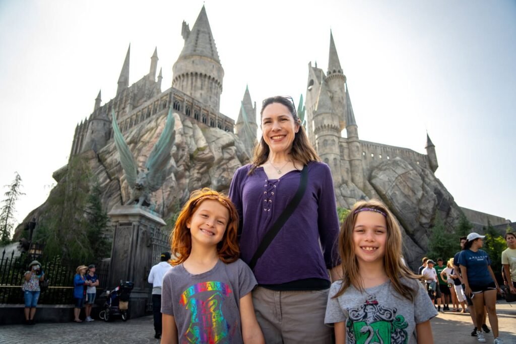 A family poses for a photo in front of the iconic castle at Hogsmeade. The setting captures the magical atmosphere of a theme park visit.