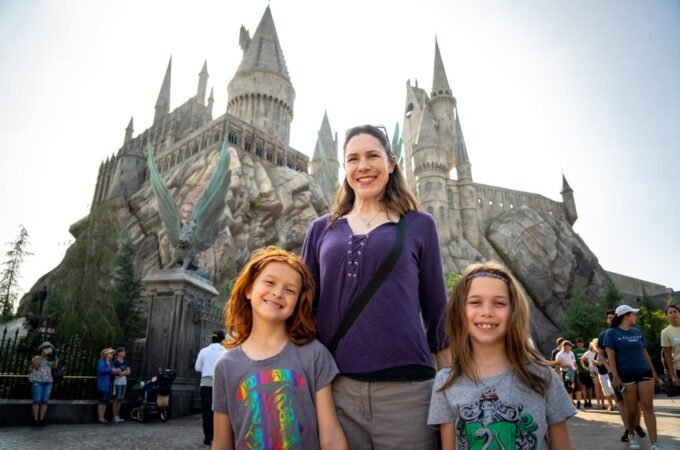 A family poses for a photo in front of the iconic castle at Hogsmeade. The setting captures the magical atmosphere of a theme park visit.