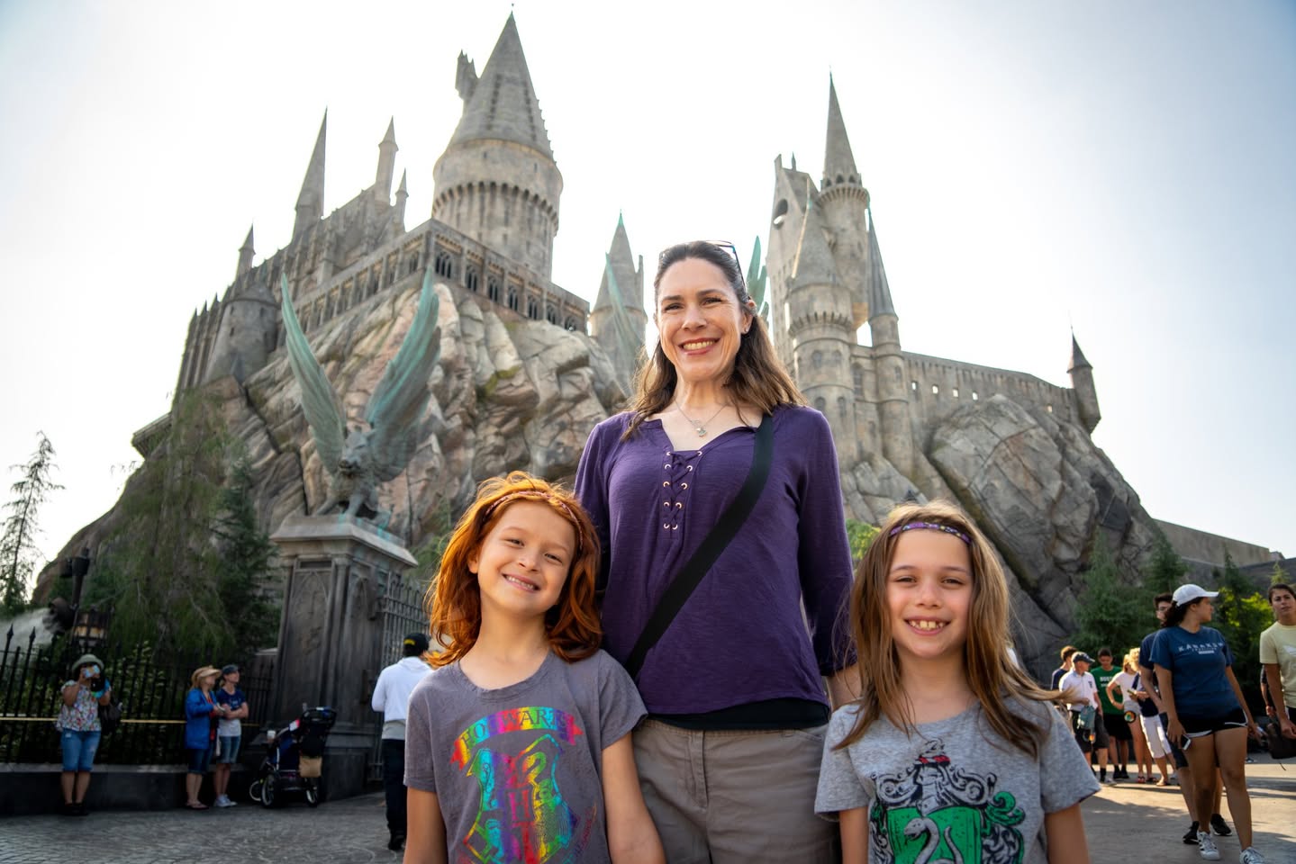 A family poses for a photo in front of the iconic castle at Hogsmeade. The setting captures the magical atmosphere of a theme park visit.
