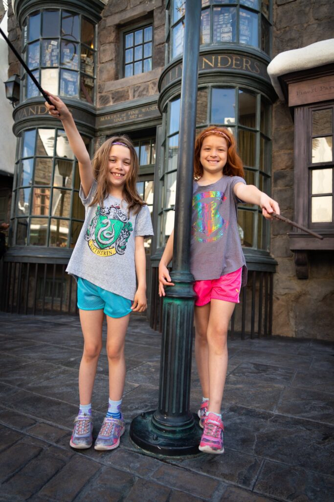 A child in a gray shirt and bright shorts holds a wand near a historic building.