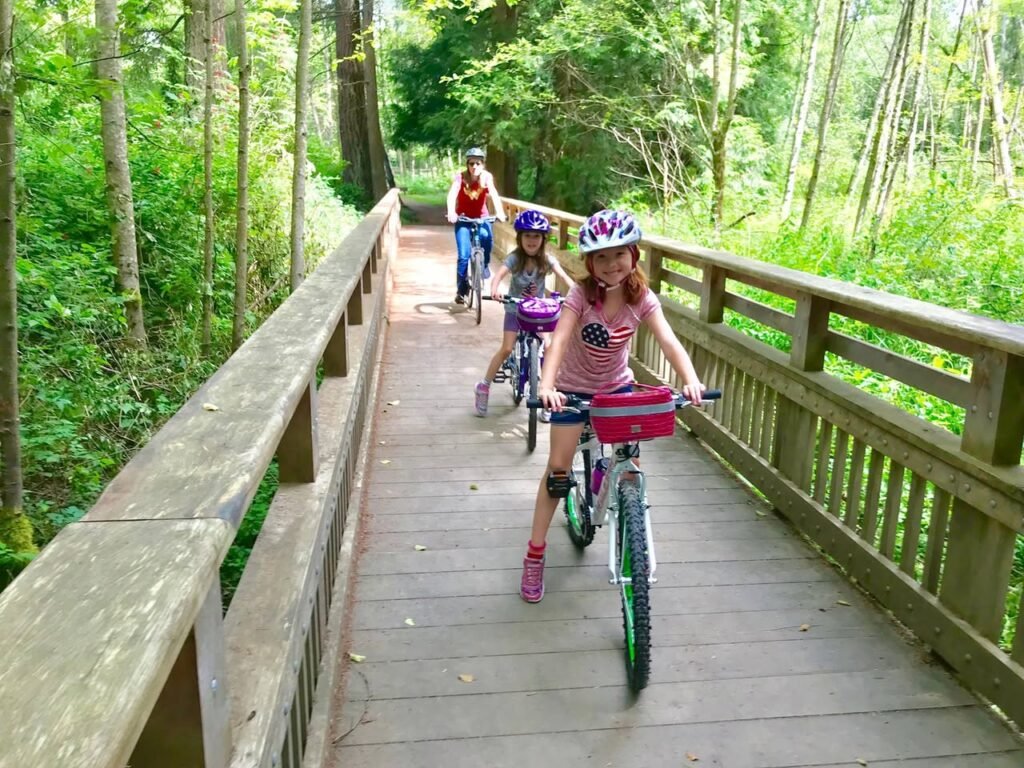 A group enjoys a bike ride on a wooden trestle bridge surrounded by lush green trees in the Pacific Northwest.