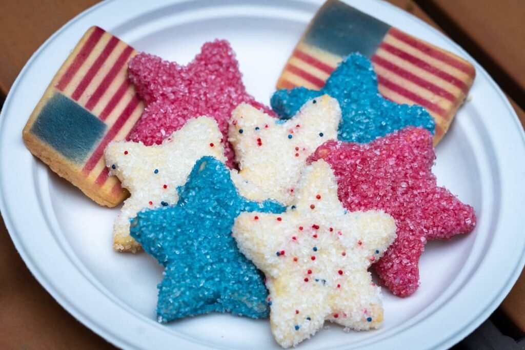 Colorful star-shaped and flag cookies decorated in red, white, and blue resting on a white plate.
