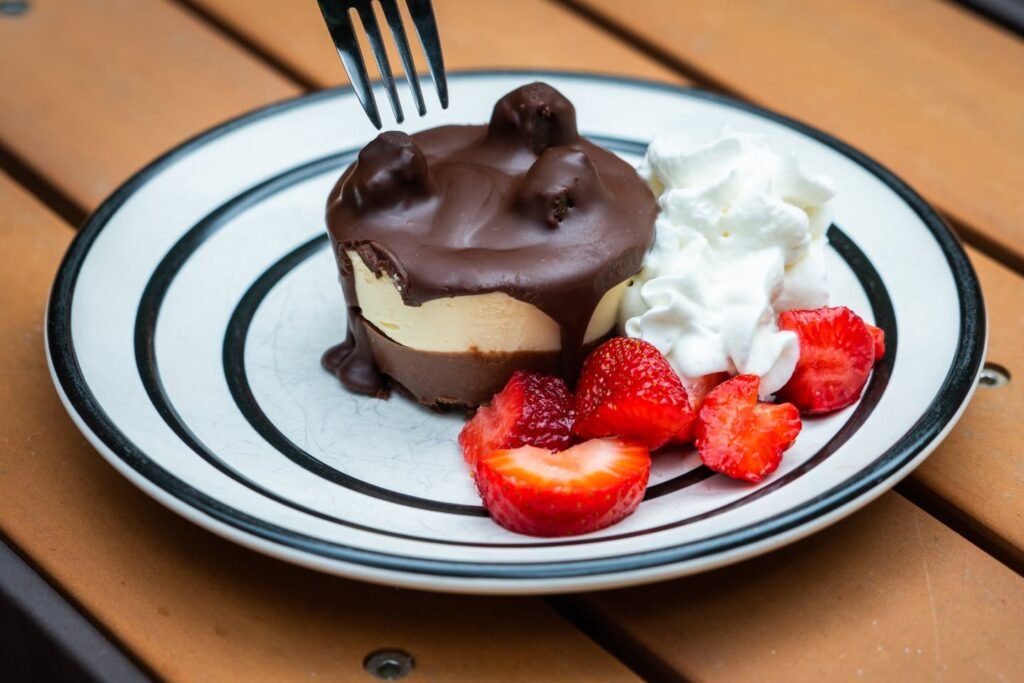 A spoon rests beside a chocolate pudding parfait on a plate, topped with fresh cream and strawberries. This close-up highlights the dessert's detail.