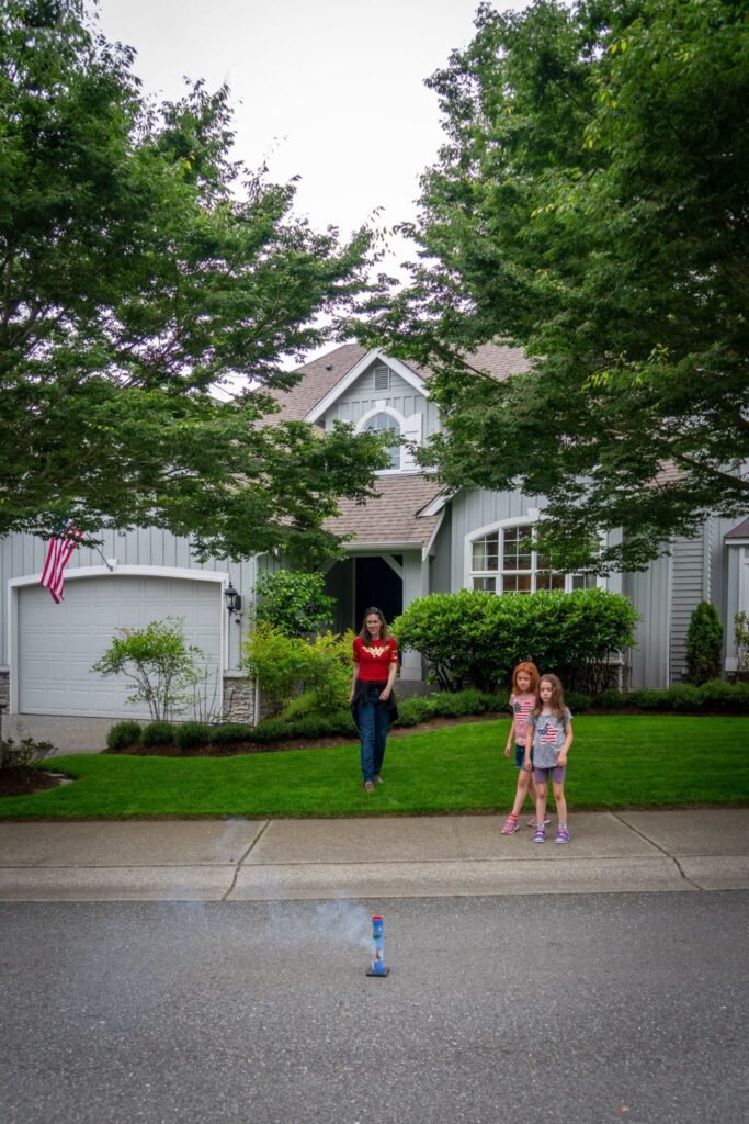 People standing in front of a large gray house with a lush green lawn and mature trees.