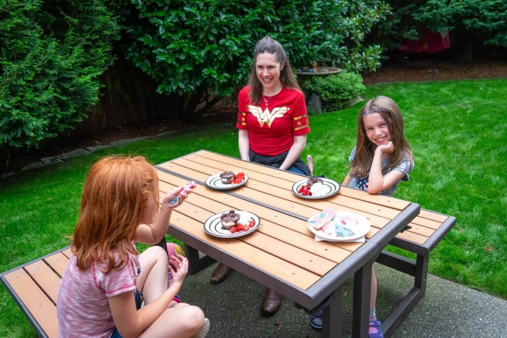 A family enjoying a meal together with plates of food on a wooden table surrounded by a beautiful natural setting.
