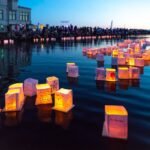 Glowing cube-shaped lanterns float on the water during an evening festival.