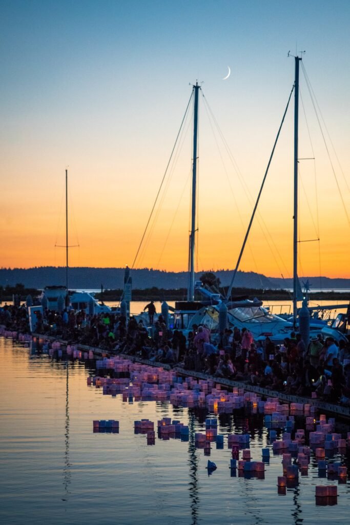 Sailboat masts and dozens of floating lanterns on the water at Salmon Bay during a sunset event in Seattle.
