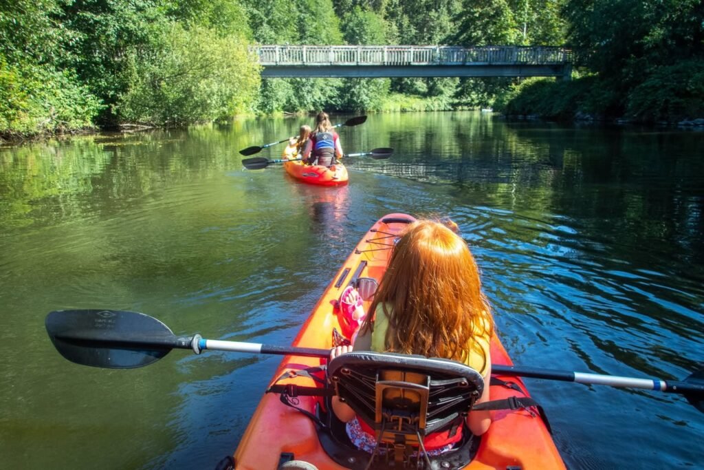 A view from a kayak on a calm, green river with a footbridge in the distance.