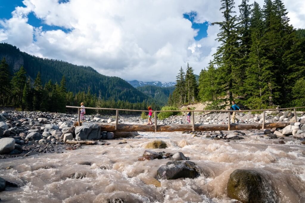 Turbulent river water rushes over rocks during a high water event. Fiercely rushing rapids flow under a bridge in a mountainous landscape.
