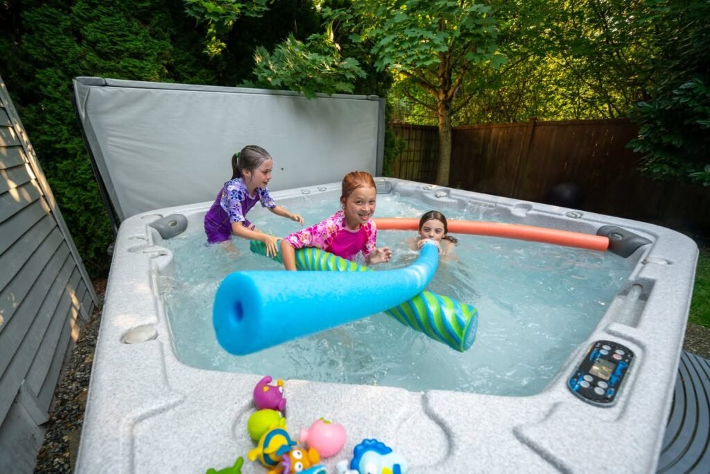 A family enjoying a hot tub with a blue noodle float. Colorful rubber ducks decorate the edge, surrounded by a wooden fence and greenery.