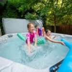 A group of kids playing in a hot tub with a water cannon and toys on the edge.
