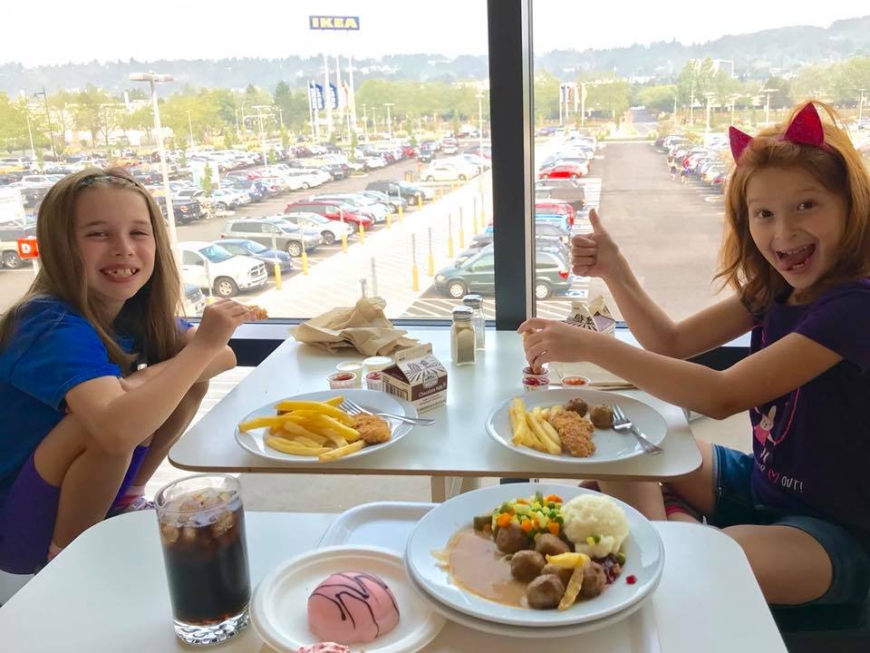 Kids enjoying a meal at a restaurant with a parking lot view in Renton. A child wears red cat ears while sharing food with a companion.