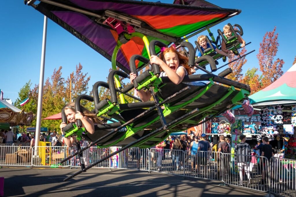 A group of people enjoy a swing ride at the state fair, with colorful canopies and a clear blue sky in the background.