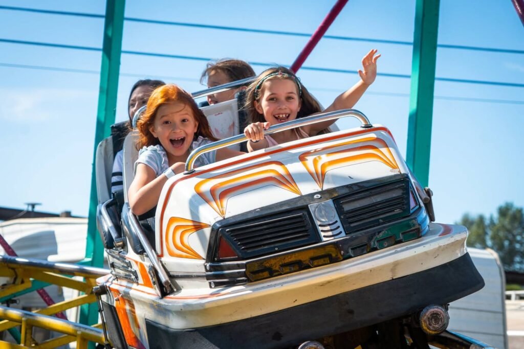 Smiling riders enjoying a car shaped theme park ride under a bright blue sky.
