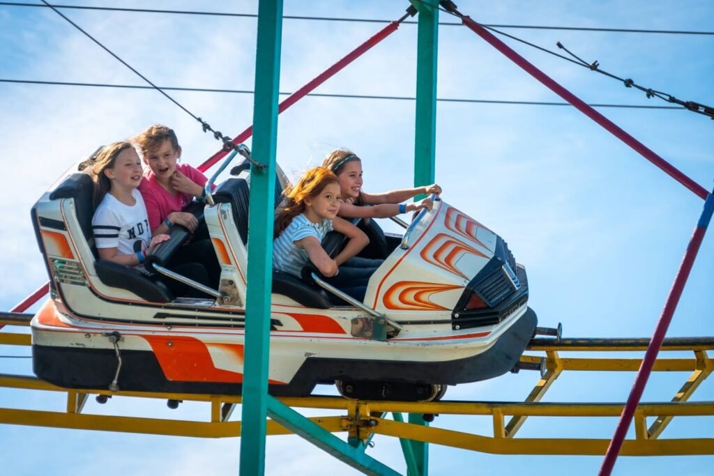 A family enjoys the thrill of a large swing ride with orange, white, and black cars against a clear blue sky.
