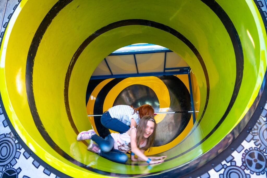 A person lies on the floor of a bright yellow spiral tube at an interactive attraction.