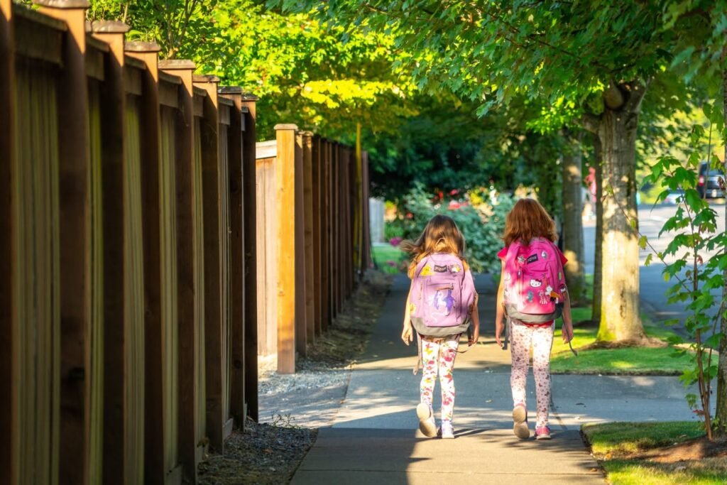 Two people walking away on a sunny sidewalk in a lush, green Pacific Northwest environment.
