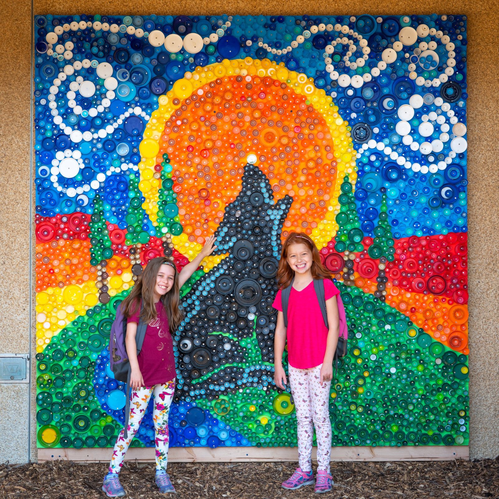 2nd Grade Two children posing in front of a colorful handcrafted mosaic art piece featuring a sun and celestial swirls.