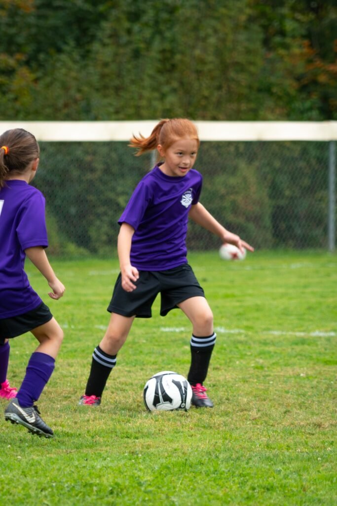 Young individuals in purple uniforms actively playing soccer on a green outfield. The focus is on the action of kicking the ball.