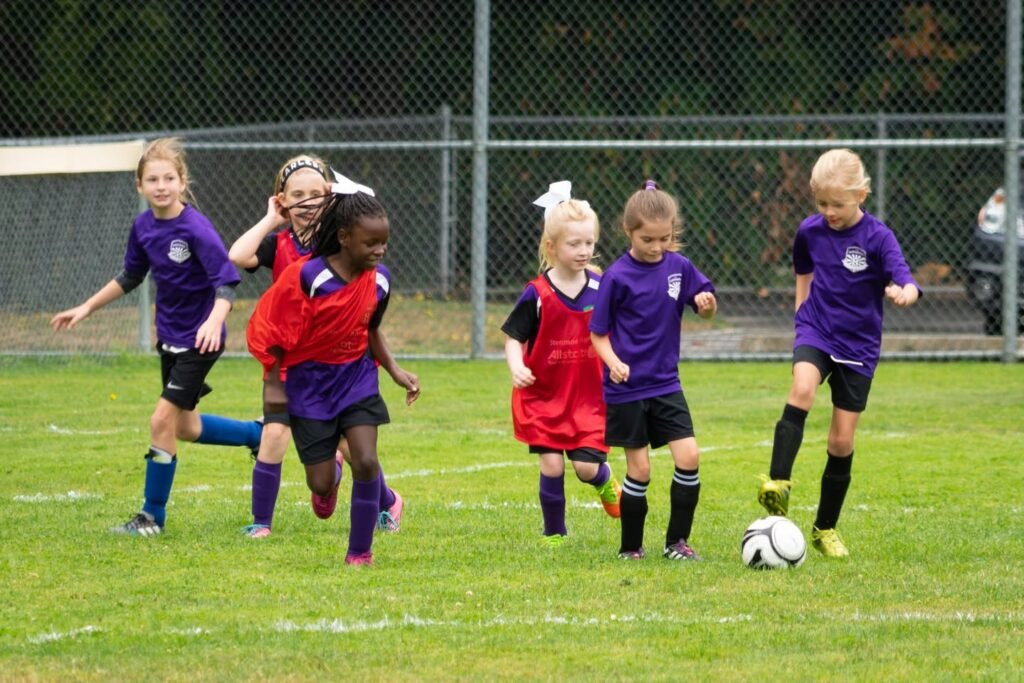 A group of young people playing soccer in purple and red uniforms on a grassy field.