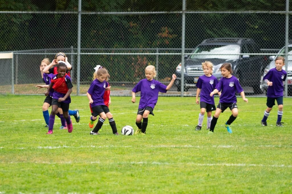 Young players in purple jerseys compete for the ball on a grassy field.