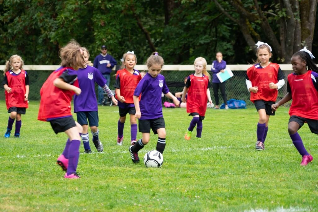 A youth soccer game in a local park, featuring players in red and purple uniforms chasing a ball.