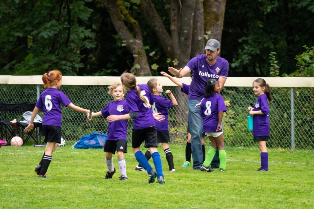 A youth soccer team in purple uniforms gathers on a grassy field during a game in the Pacific Northwest.