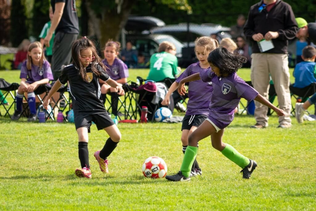 Children in purple and black uniforms compete for the ball on a grassy field during a local soccer game.