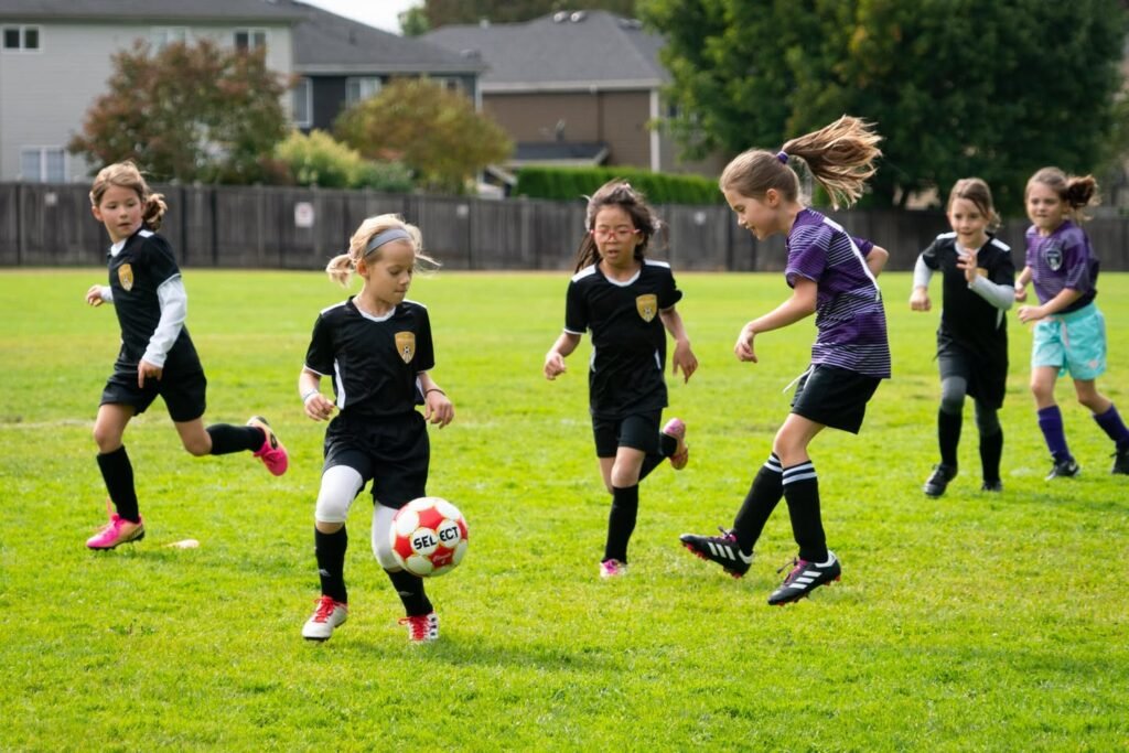 A youth soccer match in progress on a bright green field, with players in black and purple uniforms.