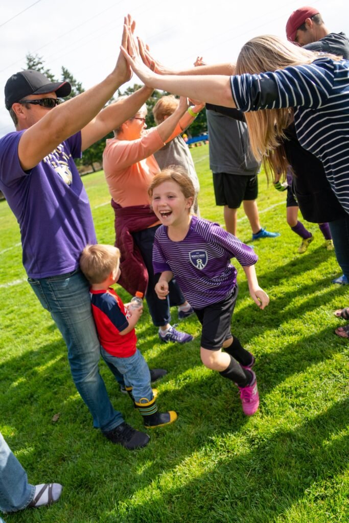 A joyful classroom of people high-fiving on a grassy field, capturing a moment of active outdoor engagement.