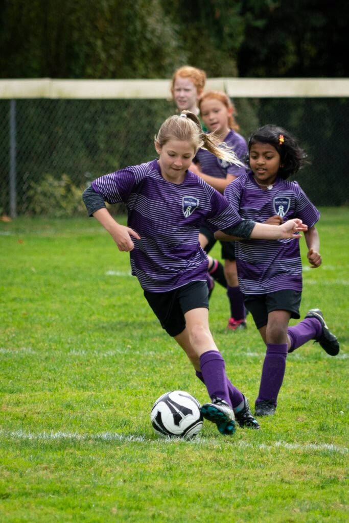 Young players in purple jerseys competing for a soccer ball on a grassy field.