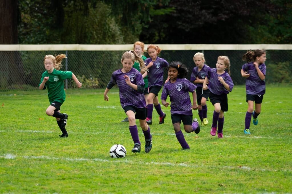 A youth soccer game with players in purple and green jerseys competing on a grassy field.