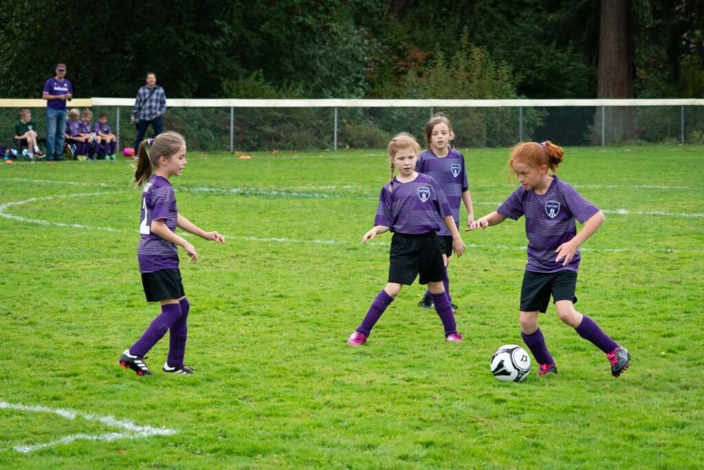 Four young players in purple uniforms compete for the ball on a green soccer field. The lower image shows close-ups of players and the action.