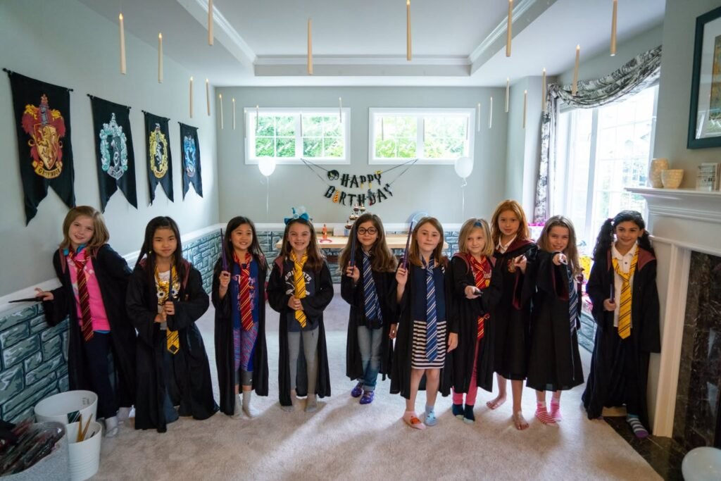 A group of children wearing Harry Potter wizard robes and ties in a decorated room with house banners.