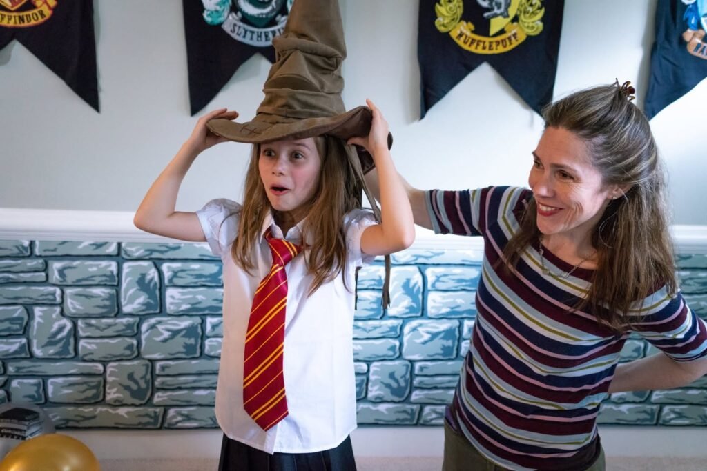 A child tries on a wizard hat while a woman smiles nearby during a Harry Potter themed party.