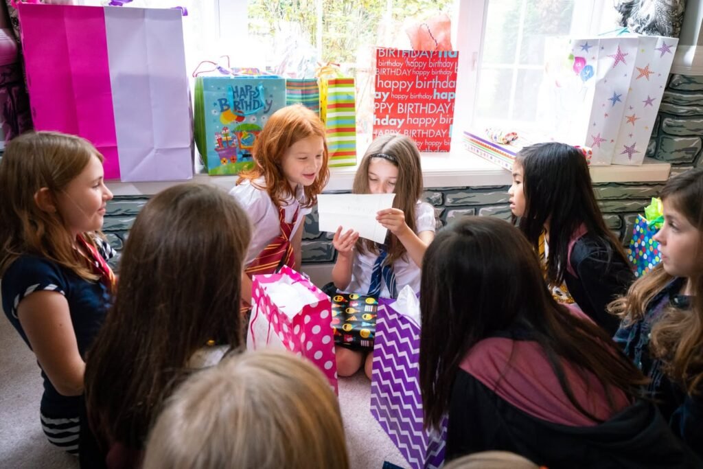 Children gather around a birthday table with colorful gift bags. The girls are seated on a bench, enjoying a fun personal moment together.