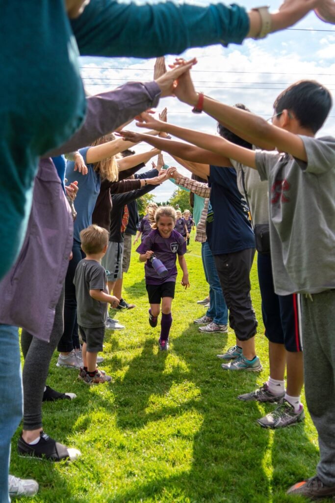 A youth runs past a high-fiving crowd of supporters on the grassy sideline, captured from a low angle near the ocean.