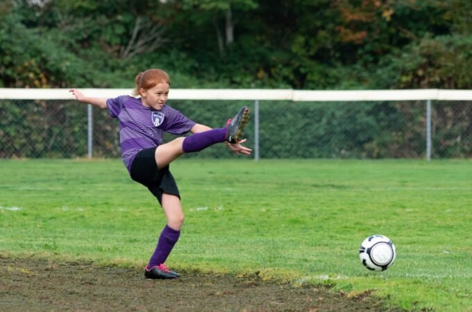 A soccer player in a purple uniform kicks a ball during an outdoor game.