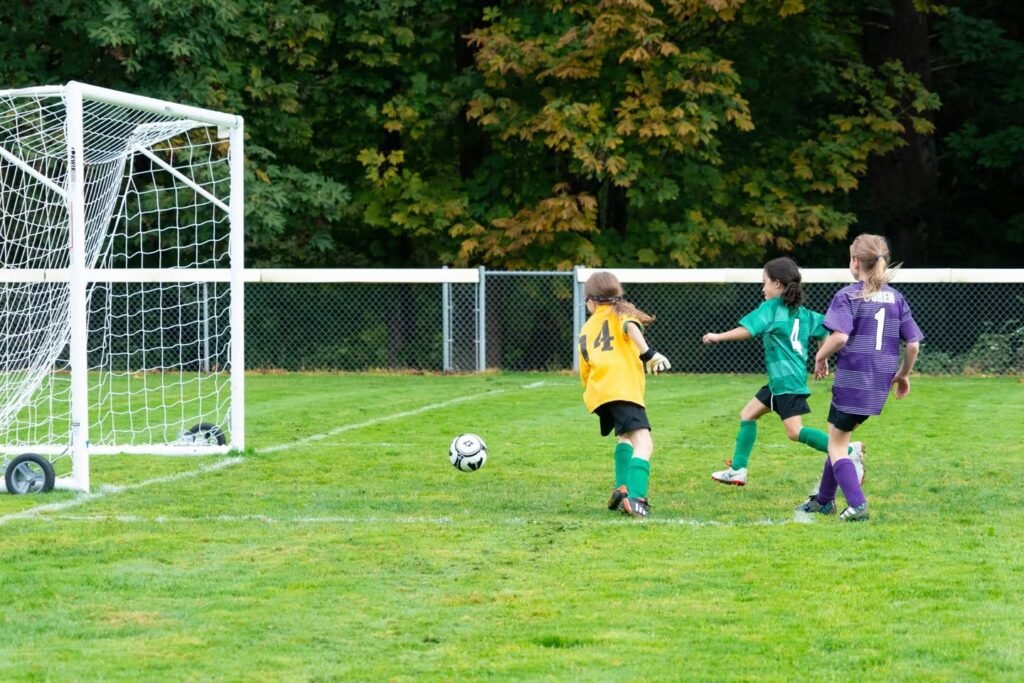 Children's soccer practice in a park with a grassy field and tall trees in the background.