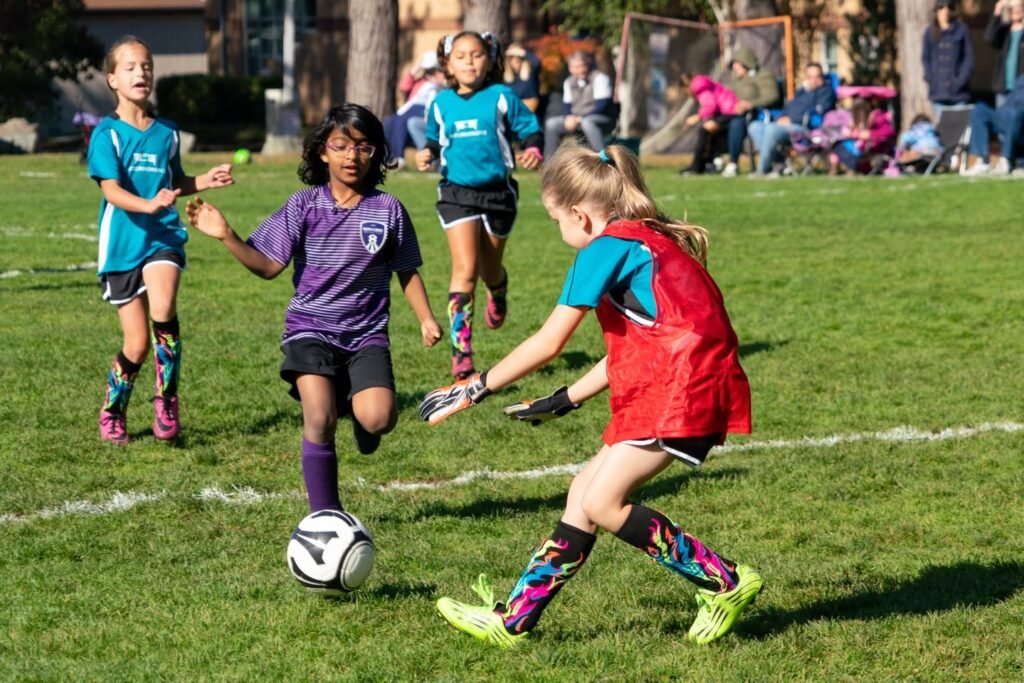 Young players in teal, purple, and red kits compete for the ball during an outdoor soccer match in the Pacific Northwest.