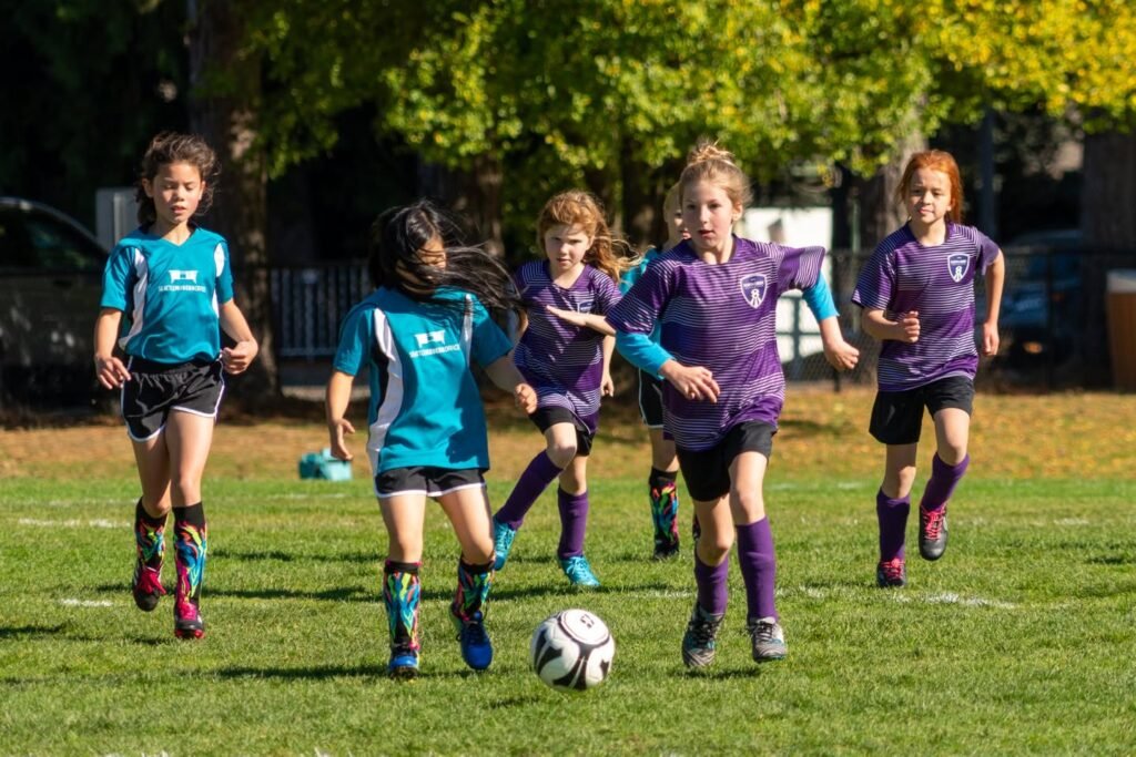 Young soccer players in purple and teal jerseys competing during a game on a grassy field.
