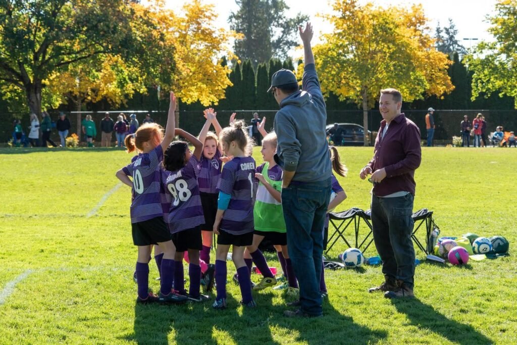 A youth soccer team celebrates with a coach on a sunny autumn field.