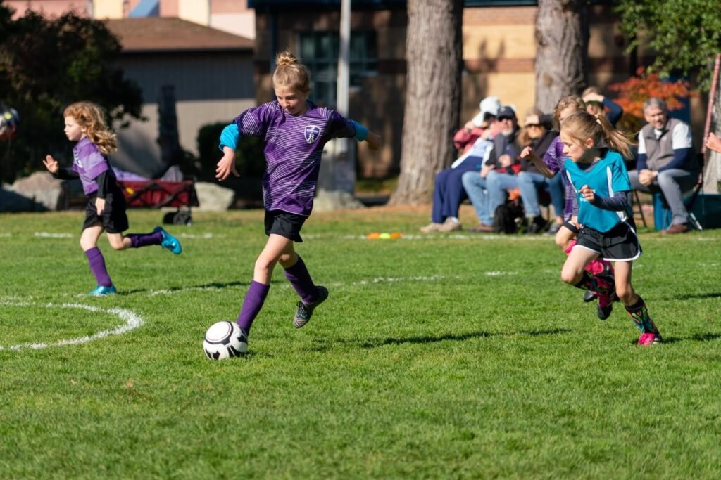 Young soccer players compete intensely on a sunny field while spectators watch from the sidelines.