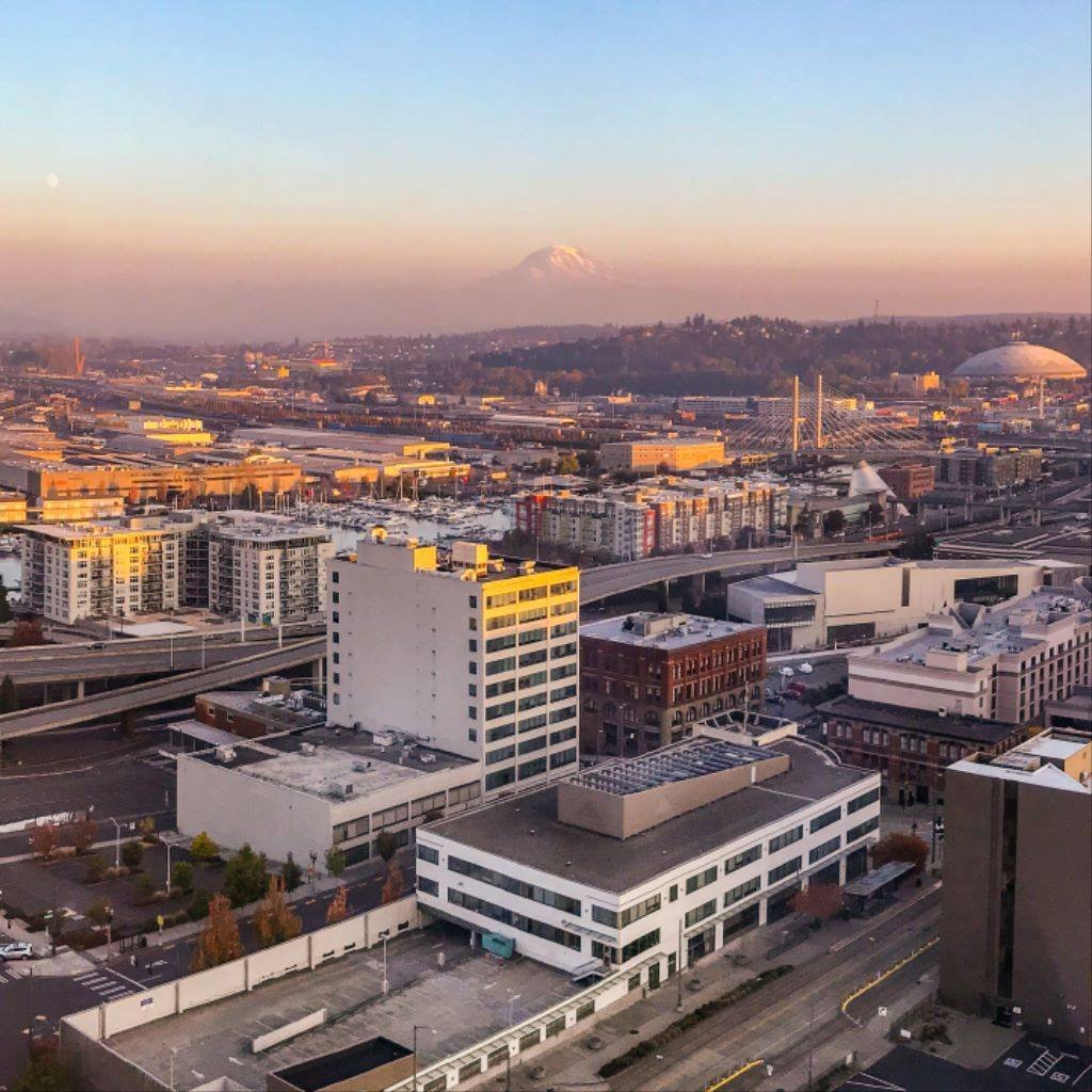 An elevated view of the Seattle skyline with modern buildings, a large domed structure, and a volcano visible on the horizon at twilight.