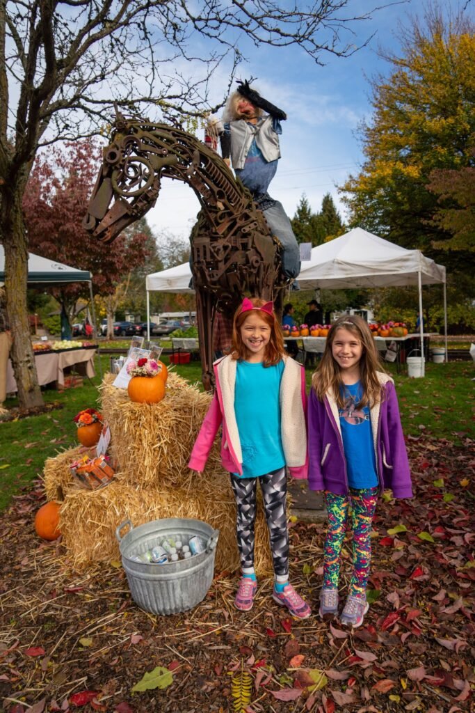 A family enjoys a autumn day at a local pumpkin patch with hay bales and a metal horse sculpture.