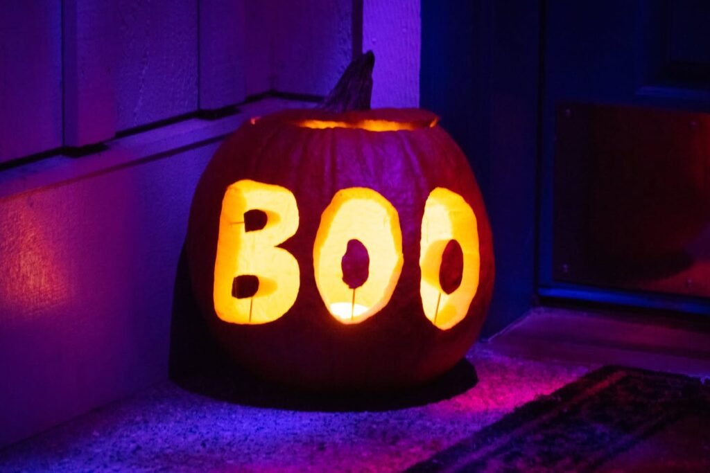 A carved pumpkin displaying the word Boo illuminated by a candle in a dark room.